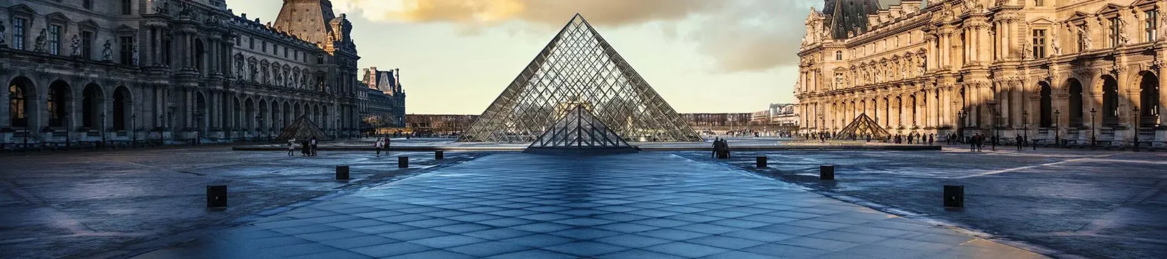 The Louvre pyramid and palace complex in Paris under bright daylight.