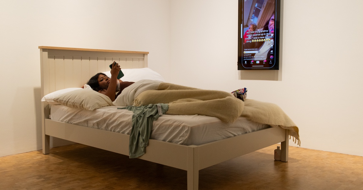 Qualeasha Wood performing from a bed within an installation environment of digital-textile works.